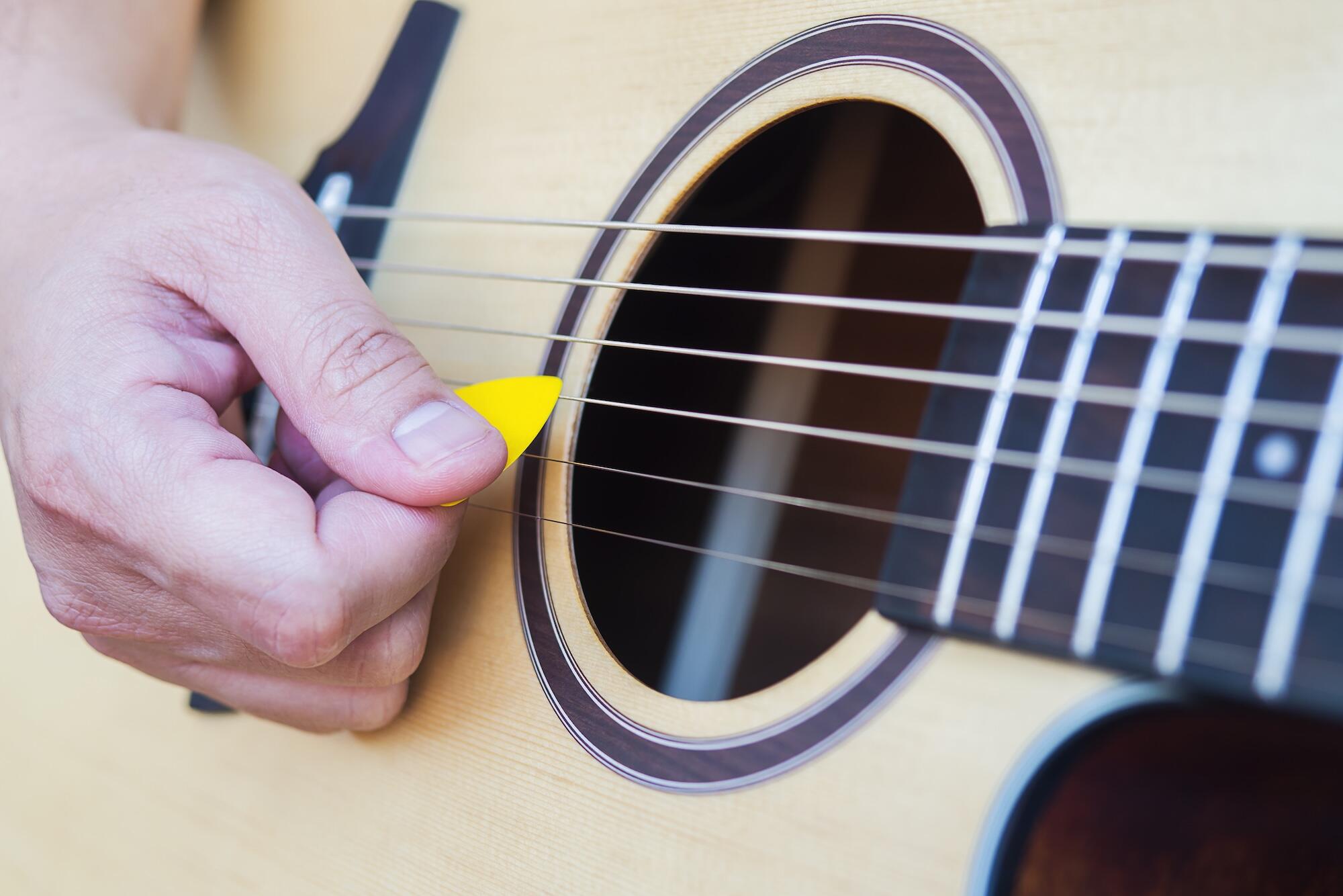Plan rapproché d'une main tenant un médiator et jouant de la guitare