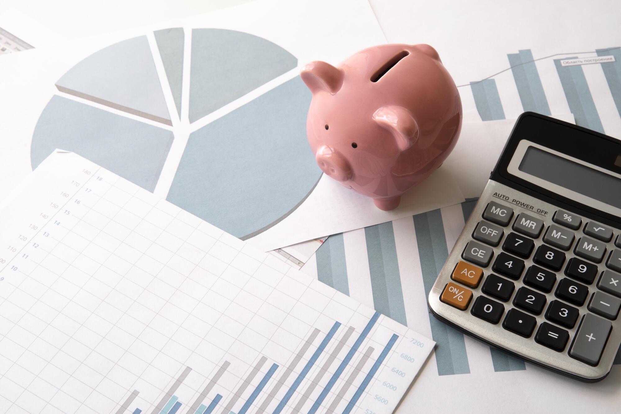 Une calculette et une tirelire sont posés sur des rapports financiers