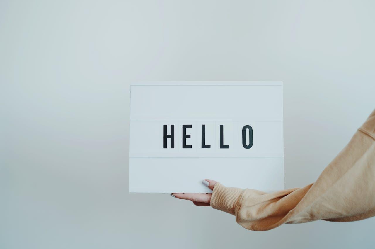 Jeune femme tenant une pancarte marquée "Hello" (bonjour). On ne voit que son bras tendu. 