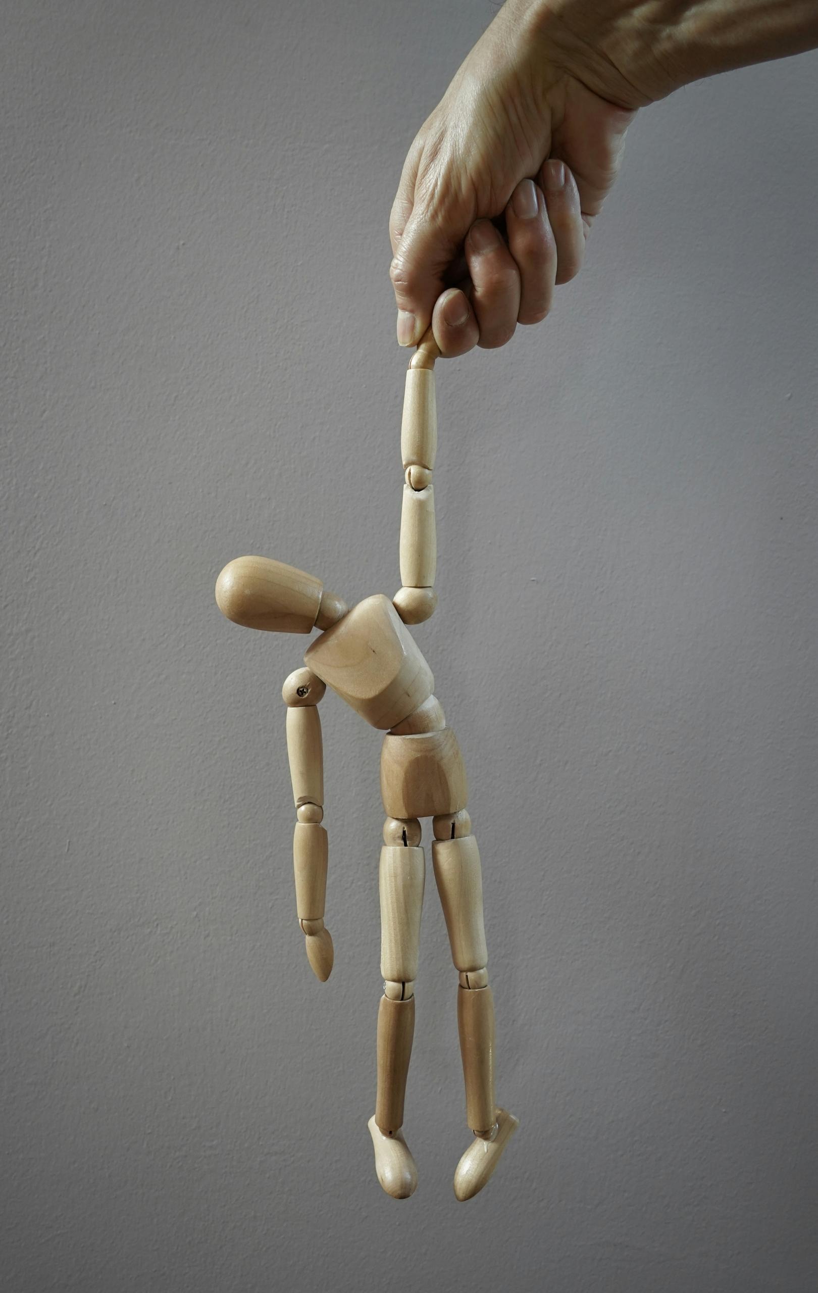 Un pantin en bois tenu par une main.