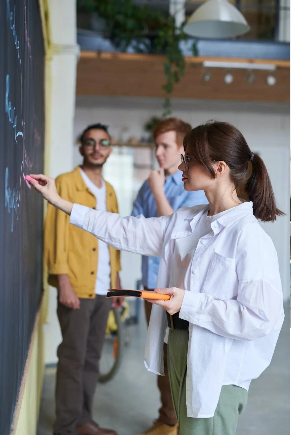 Une élève écrit au tableau aux côtés de son enseignant.