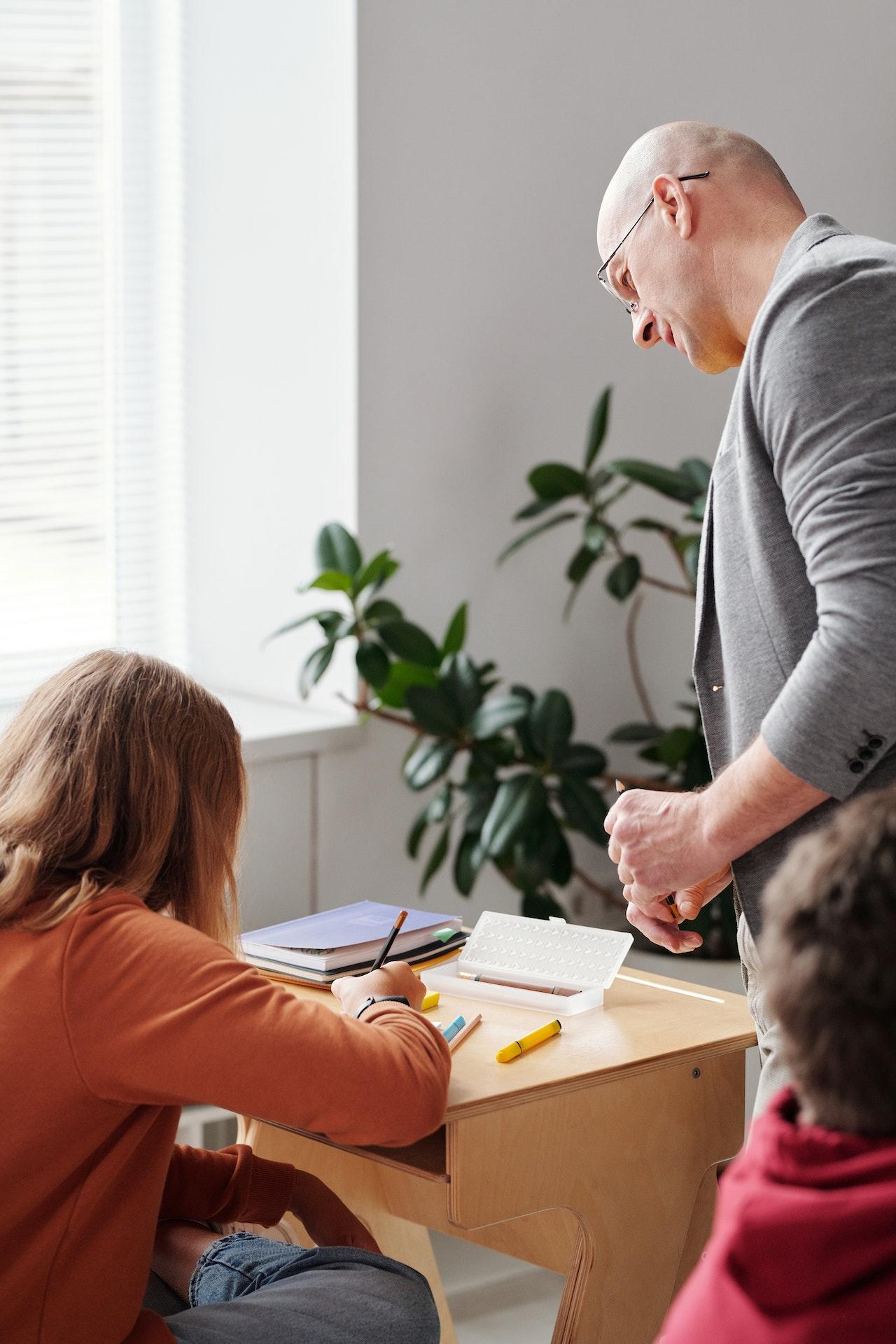 Professeur regardant ce que fait une élève assise à son bureau.