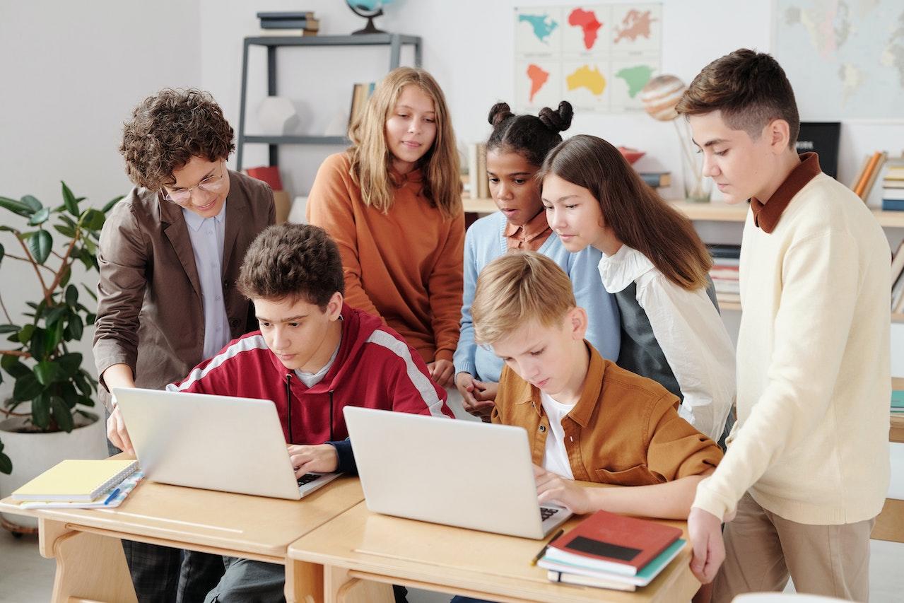 Classe avec plusieurs élèves et professeur devant deux ordinateurs.