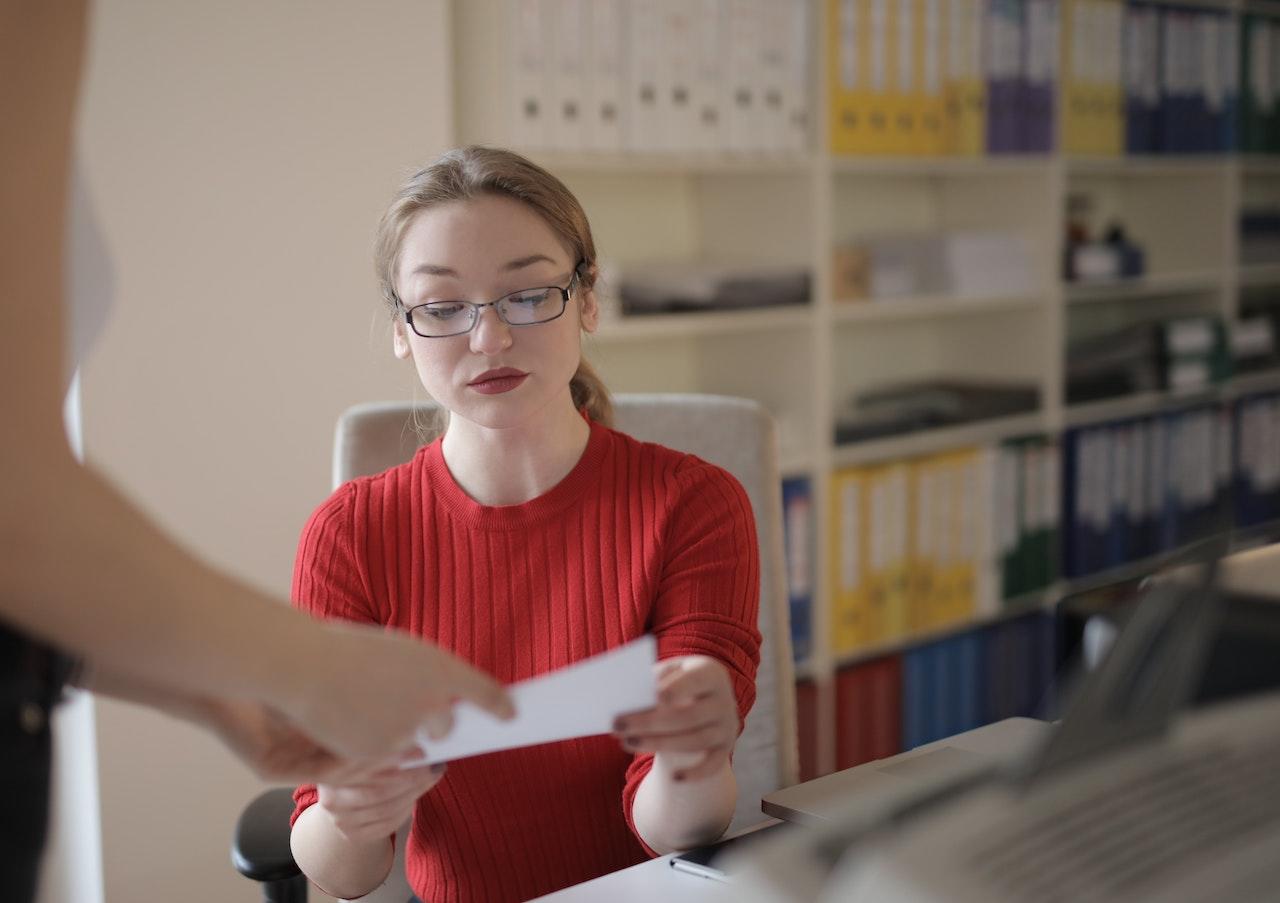 Jeune professeure assise devant un ordinateur portable et recevant un papier des mains de l'inspecteur académique.