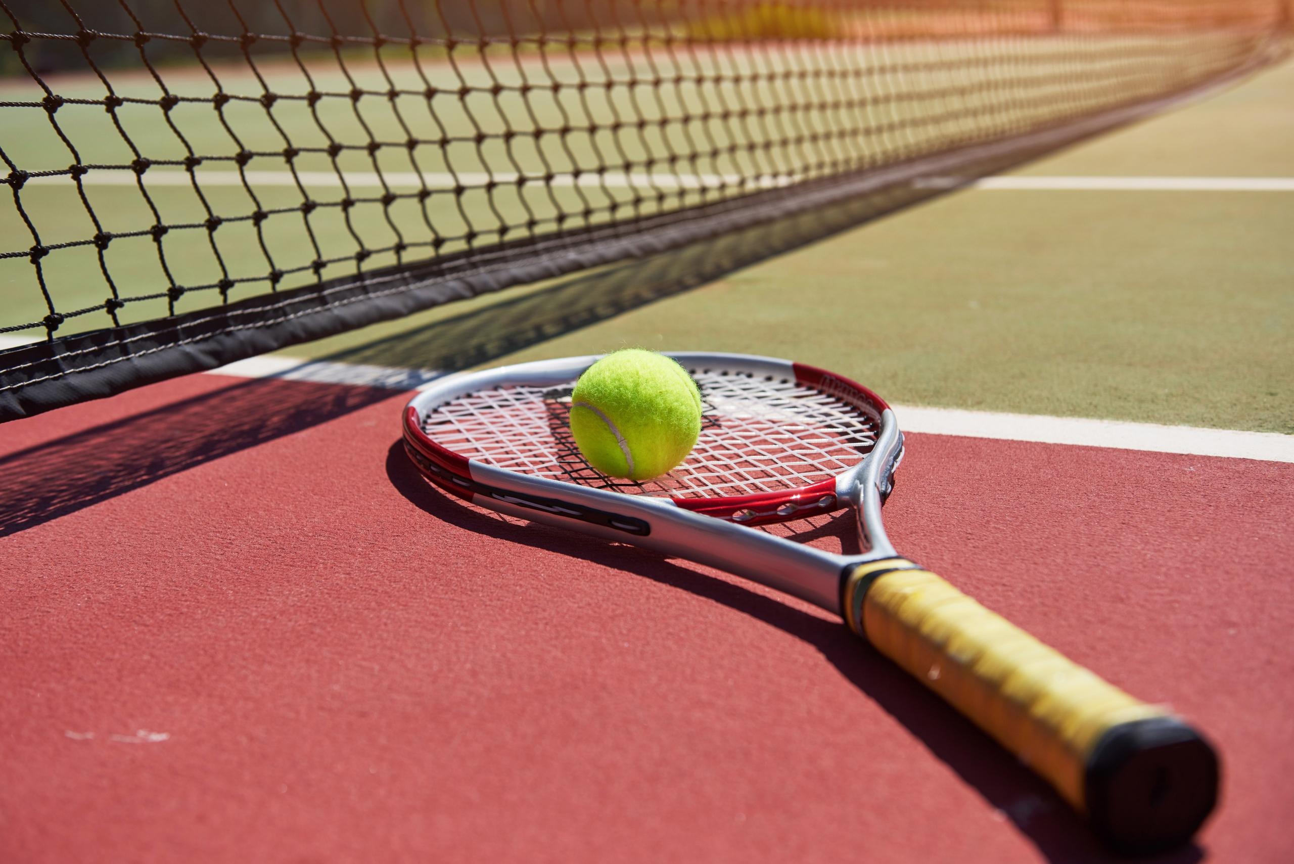 une raquette de tennis posée au sol sur un terrain de tennis. Une balle est sur la raquette.
