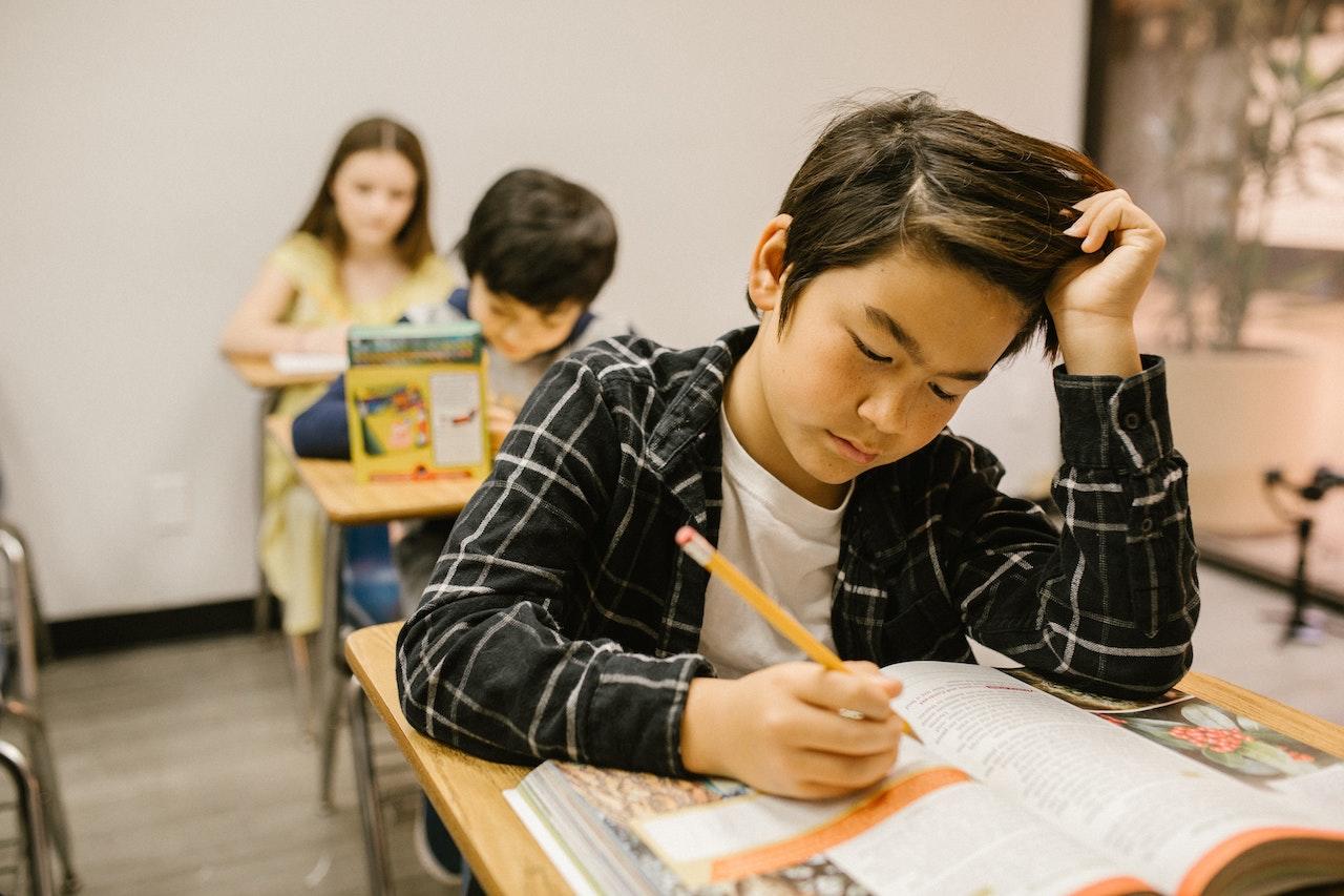 Enfant asiatique en classe qui essaie de comprendre un texte dans un livre. Il a un crayon à la main. 
