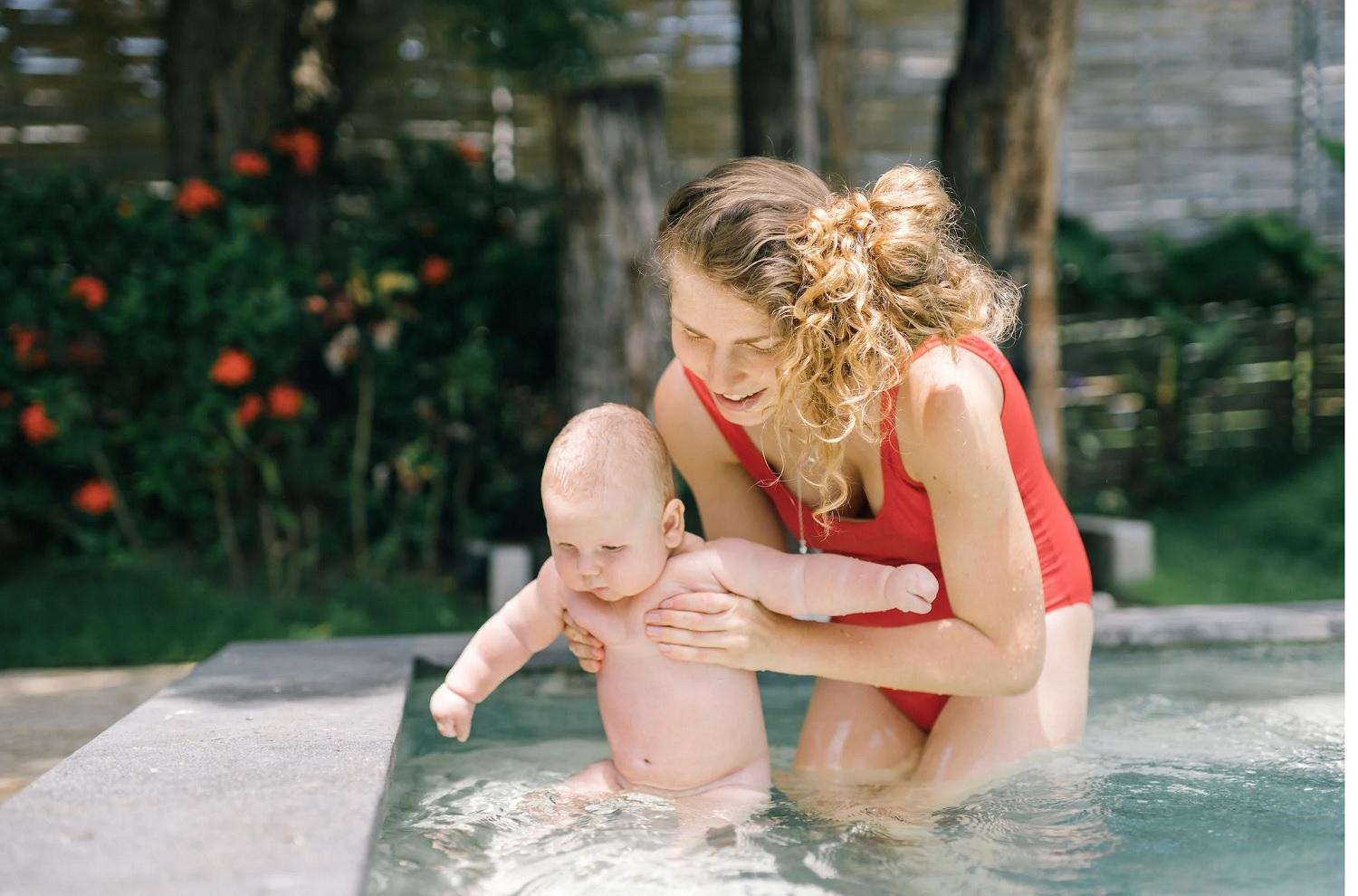 Une mère aide son bébé à entrer dans l'eau.