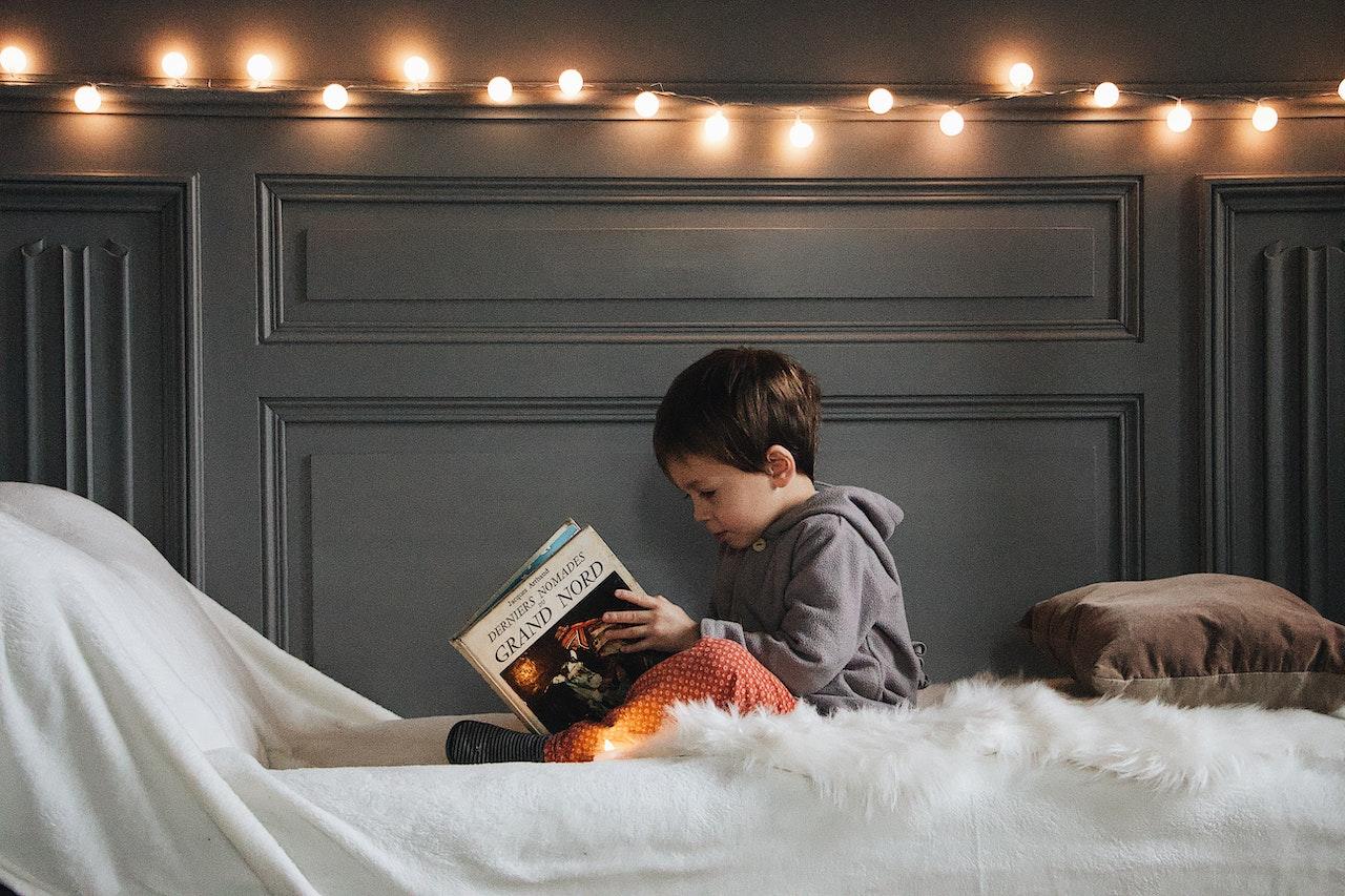 Jeune garçon dyslexique assis sur un lit, un livre entre les mains intitulé "Les Derniers Nomades du Grand Nord".