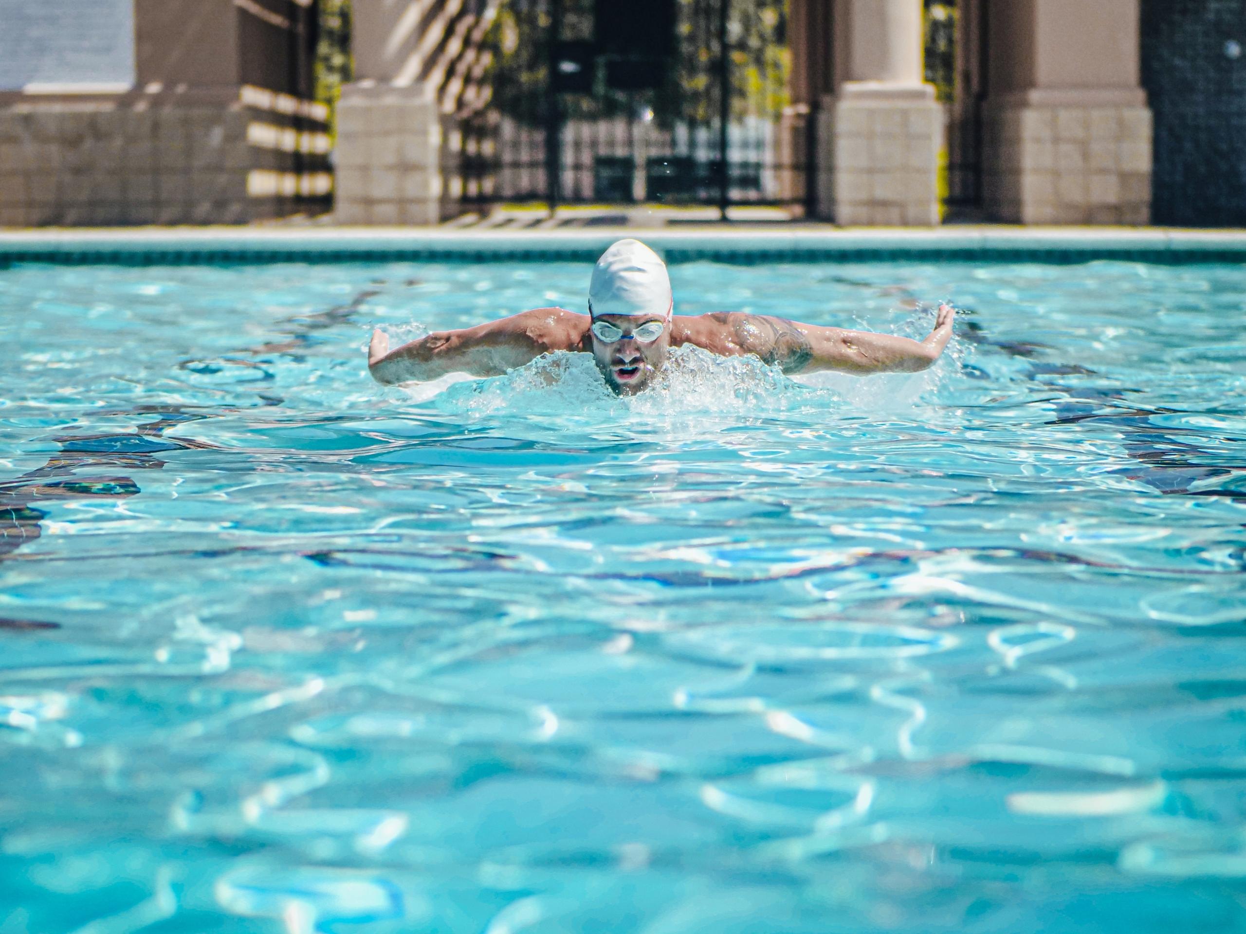 nageur avec bonnet blanc pratiquant le papillon dans une piscine ouverte