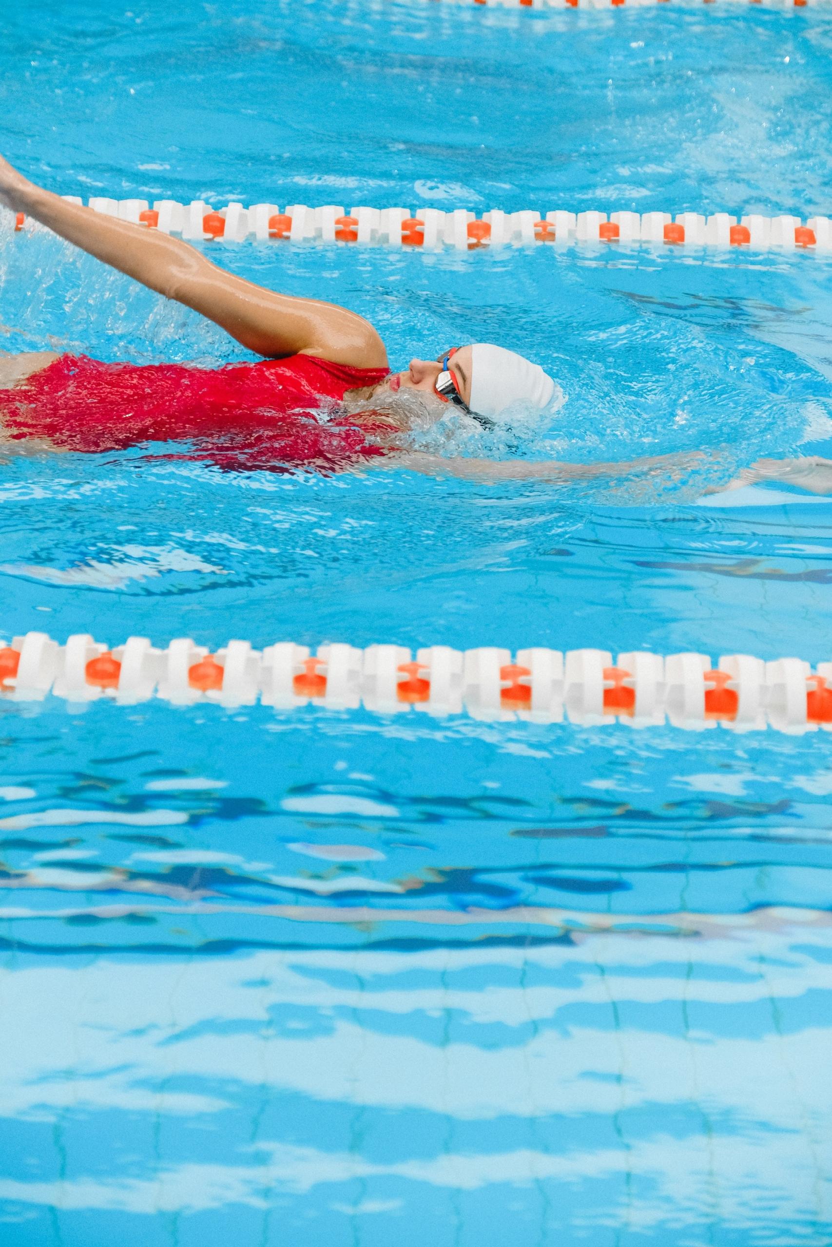 nageuse pratiquant la nage dorsale avec maillot de bain rouge dans une piscine
