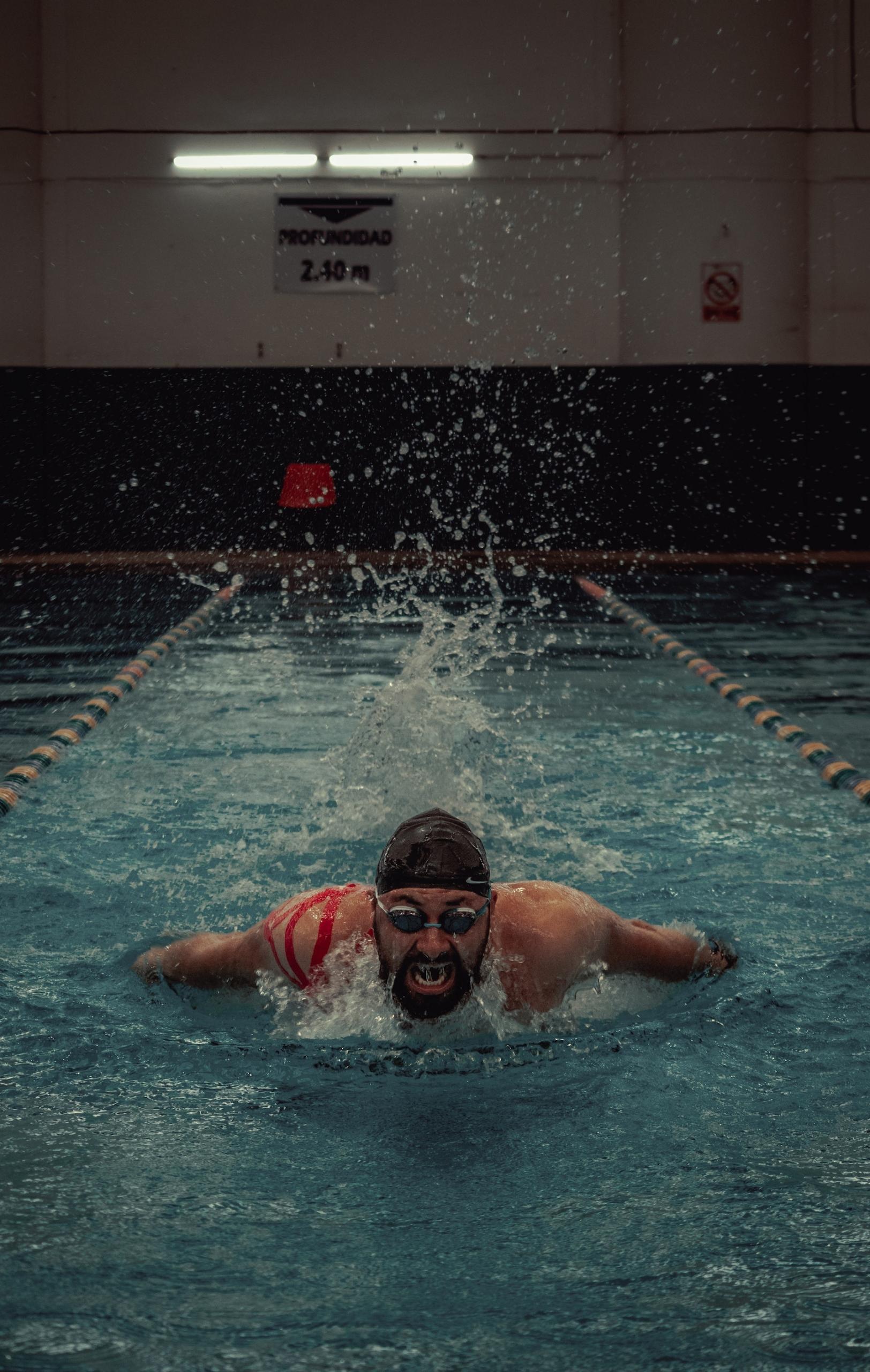 nageur avec bonnet pratiquant le papillon dans une piscine fermée