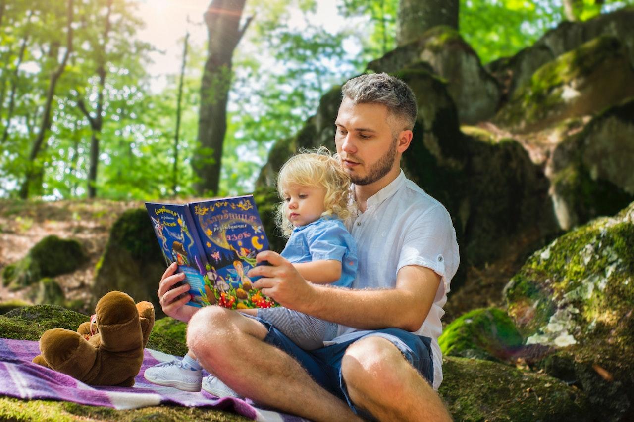 Père lisant un livre à sa fille assise sur ses genoux dans une forêt. 