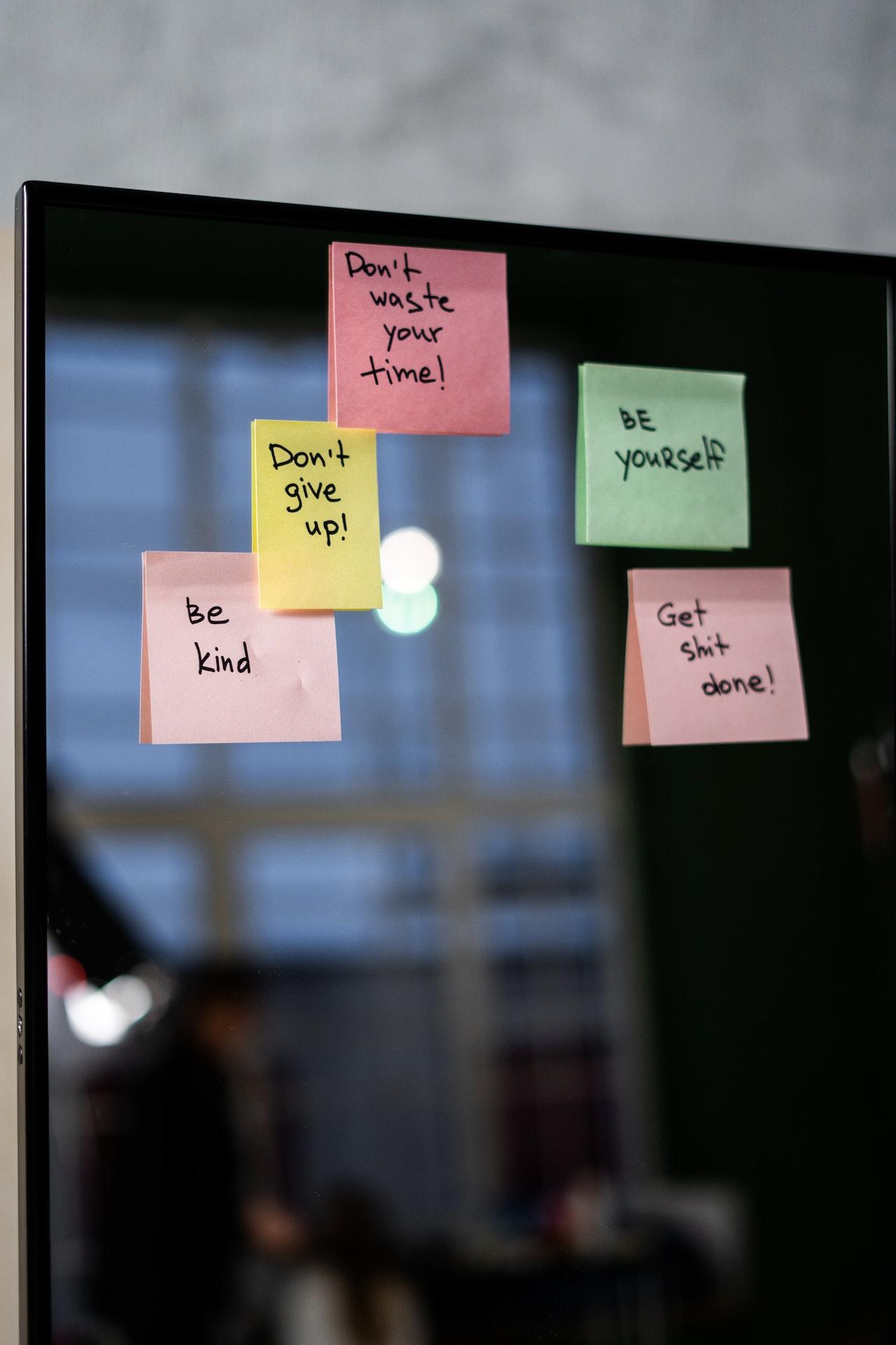 Ecran d'ordinateur sur lequel sont apposés des post-it en anglais : don't waste your time, bee yourself, don't give up, be kind, get shit done.
