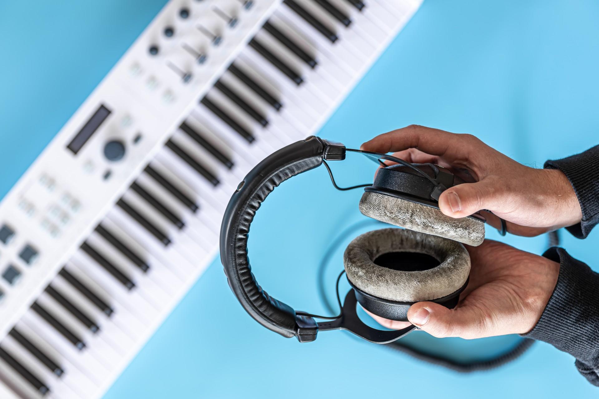 2 mains qui tiennent un casque audio avec un synthétiseur en arrière-plan.