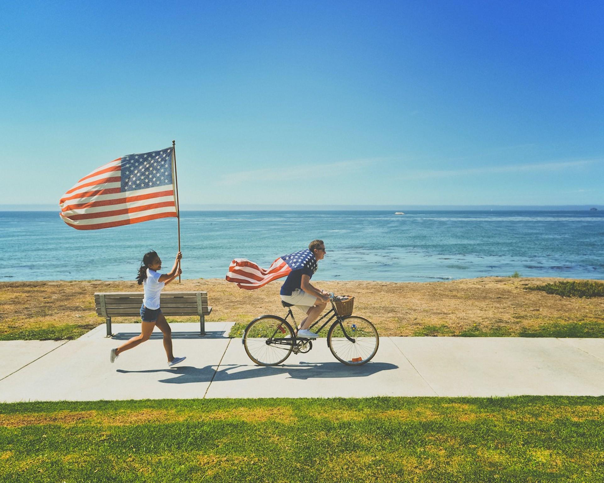 1 personne à vélo et 1 personne qui court derrière avec drapeau américain.
