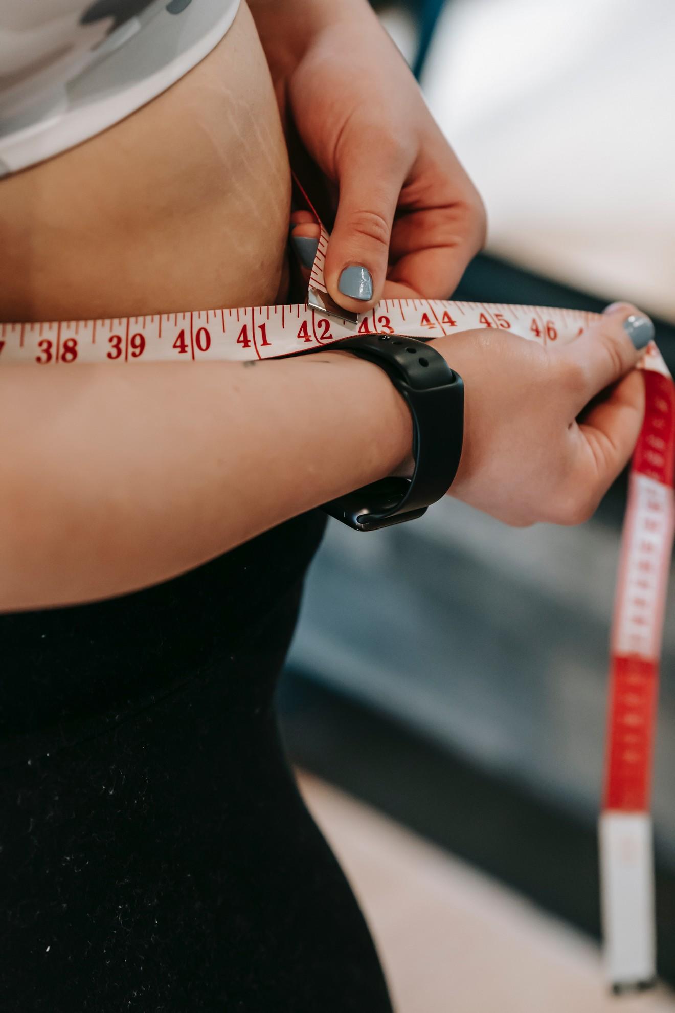 Quelqu'un en train de mesurer son tour de taille avec un mètre ruban.