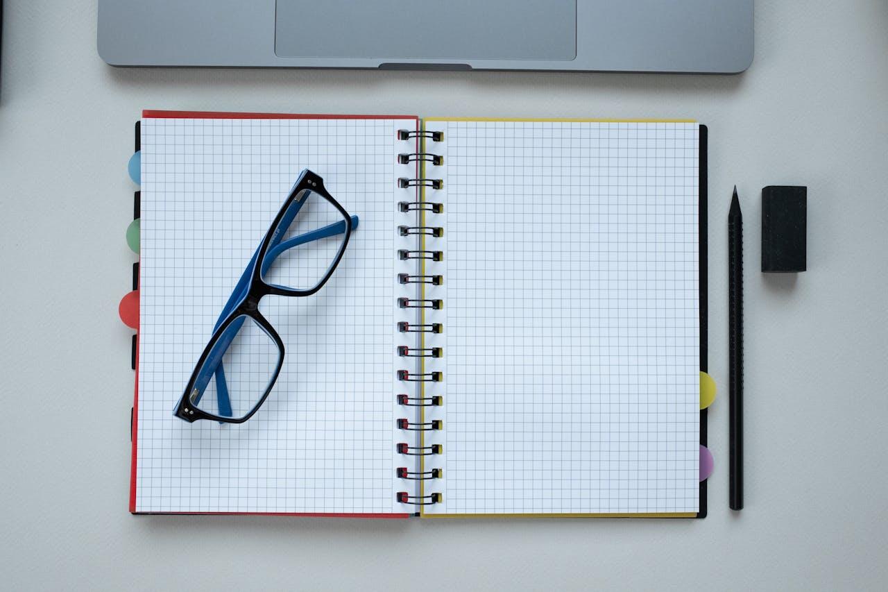 lunettes posees sur carnet sur une table a cote d un crayon et devant un laptop