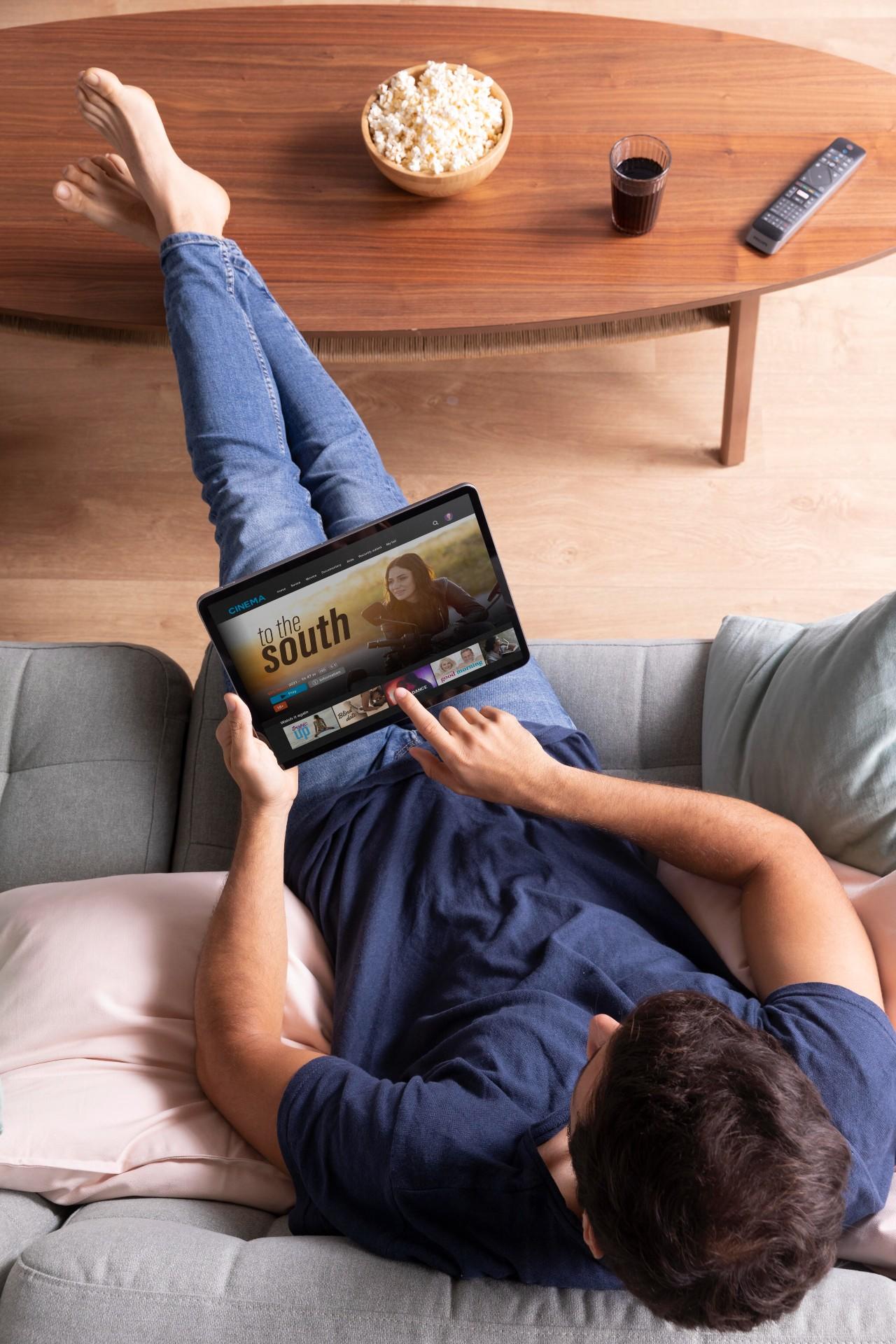 Un homme dans son canapé regardant une série sur sa tablette.