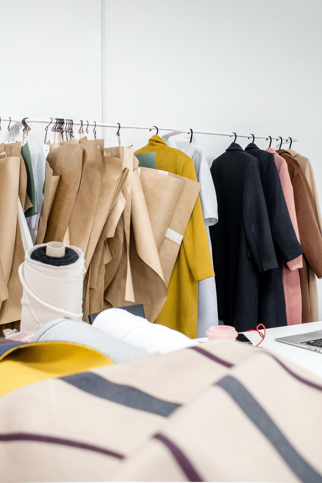 Un portant à vêtement avec une multitude de vestes et échantillons de tissus.