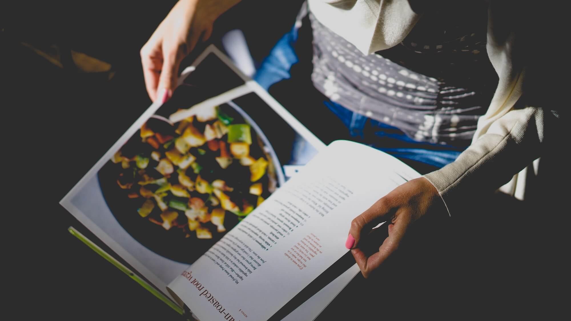 Personne qui tient un livre de recettes dans ses mains.