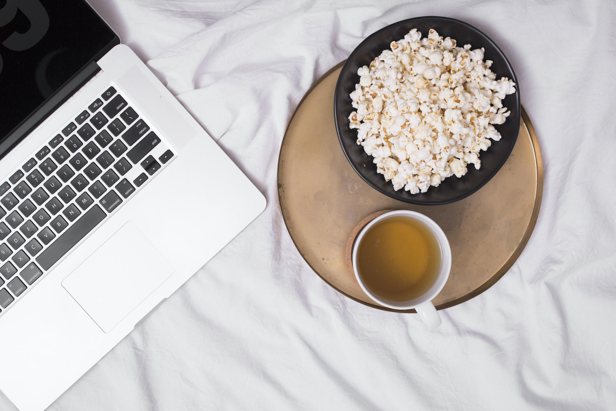 Un bol de popcorn avec un thé et un ordinateur posé sur un lit.