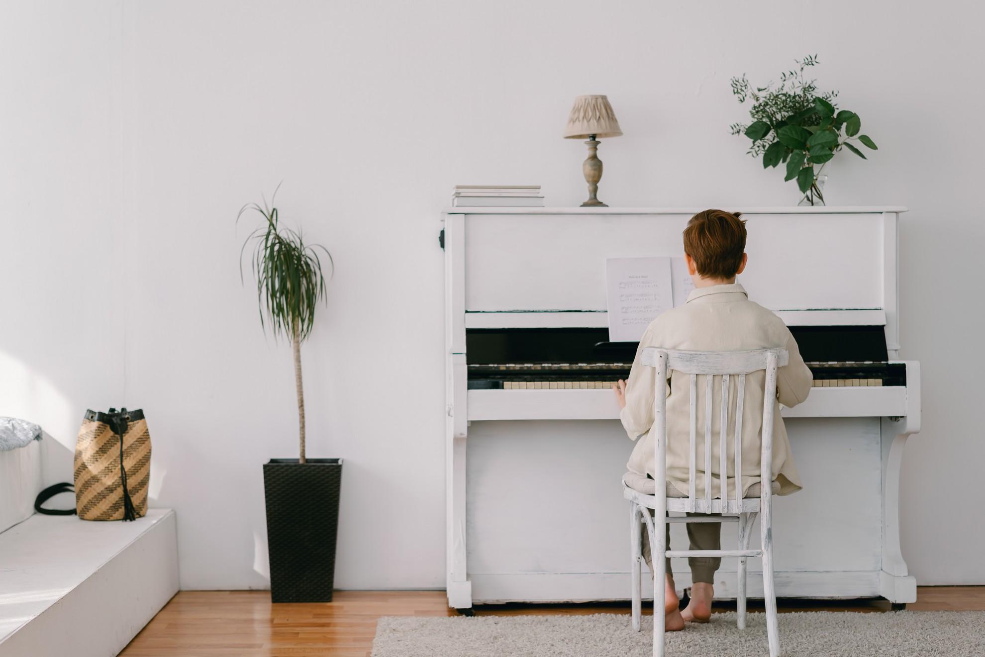 Un jeune garçon jouant sur un piano blanc entouré de plantes vertes.