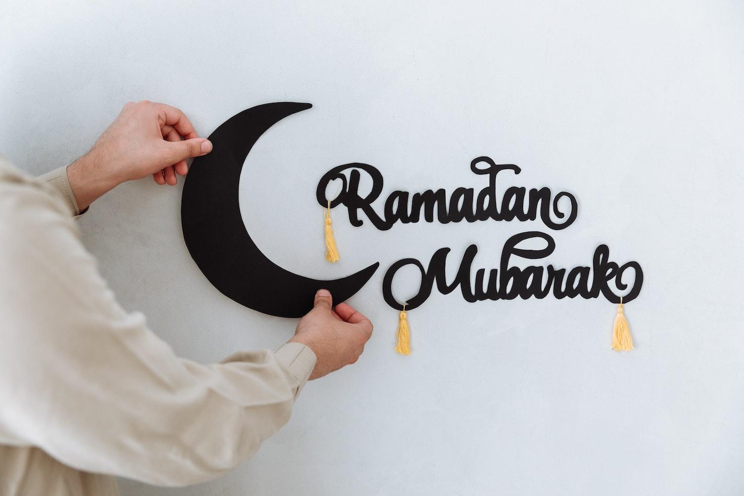 Une personne est en train d'installer une décoration de lune à côté du mot Ramadan Mubarak.
