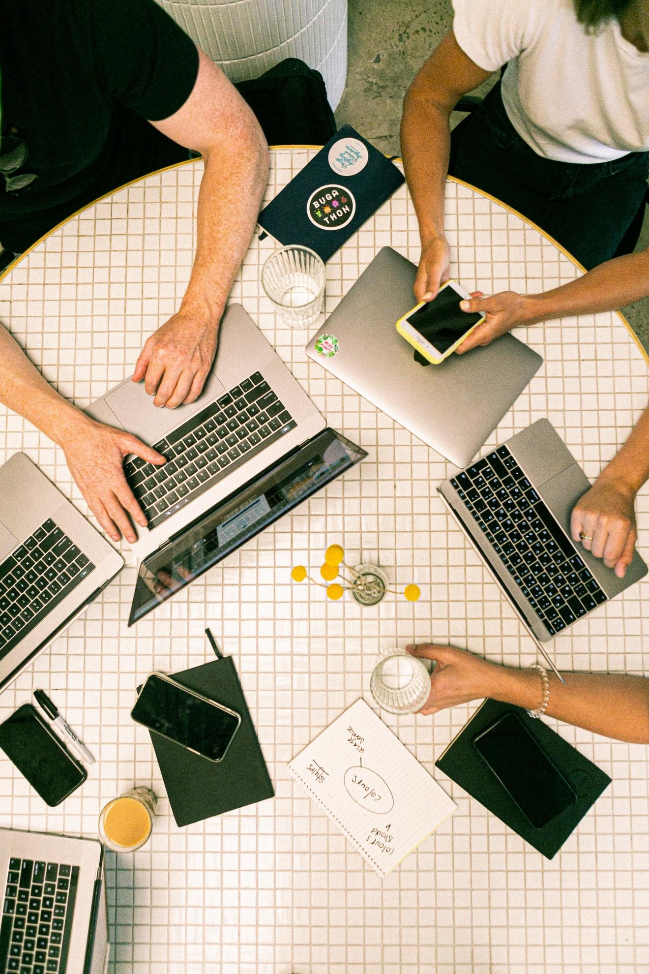 Des personnes en train de travailler en groupe sur différents ordinateurs et smartphones.