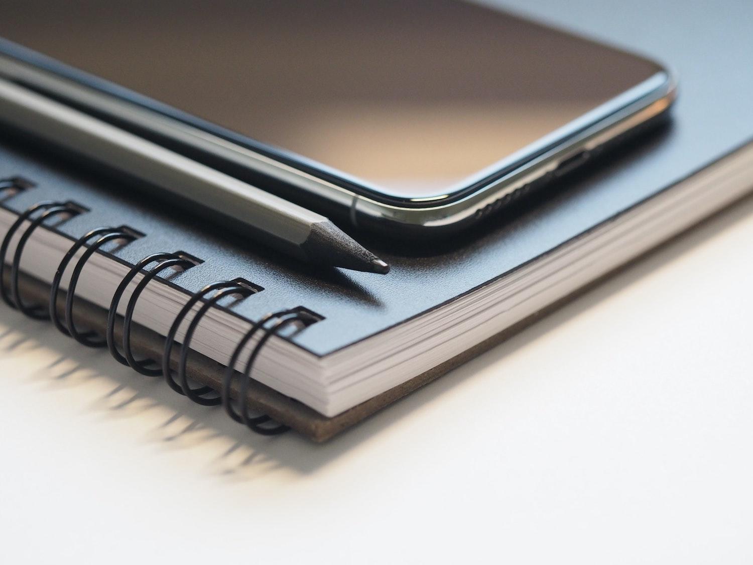 Un téléphone portable et un stylo sont posés sur un carnet à spirales.