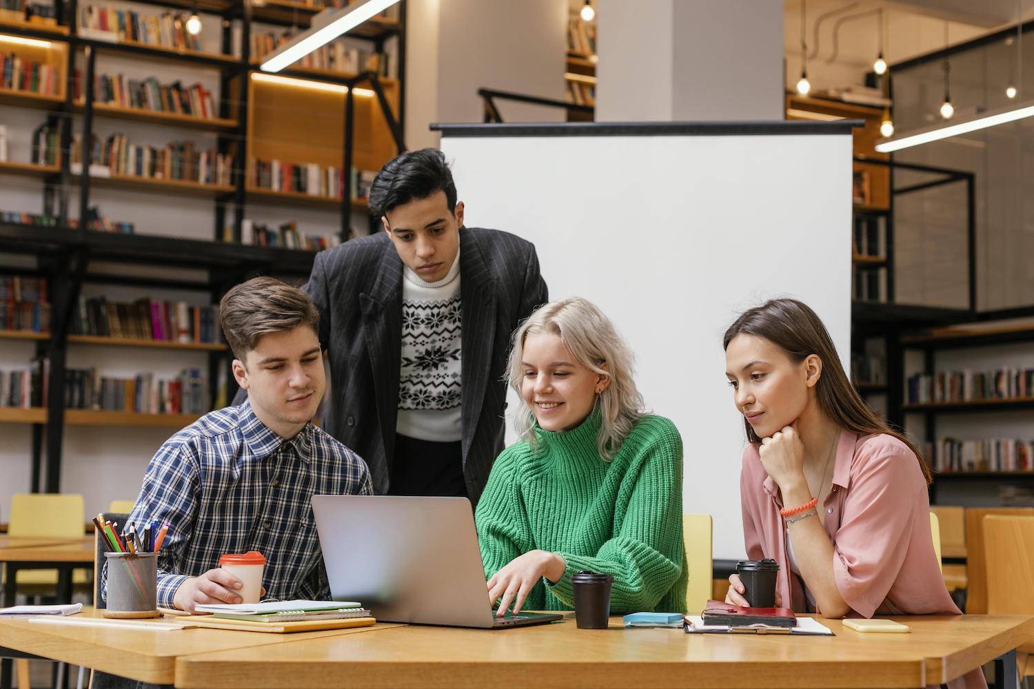 4 étudiants sont rassemblés devant un ordinateur dans une bibliothèque.