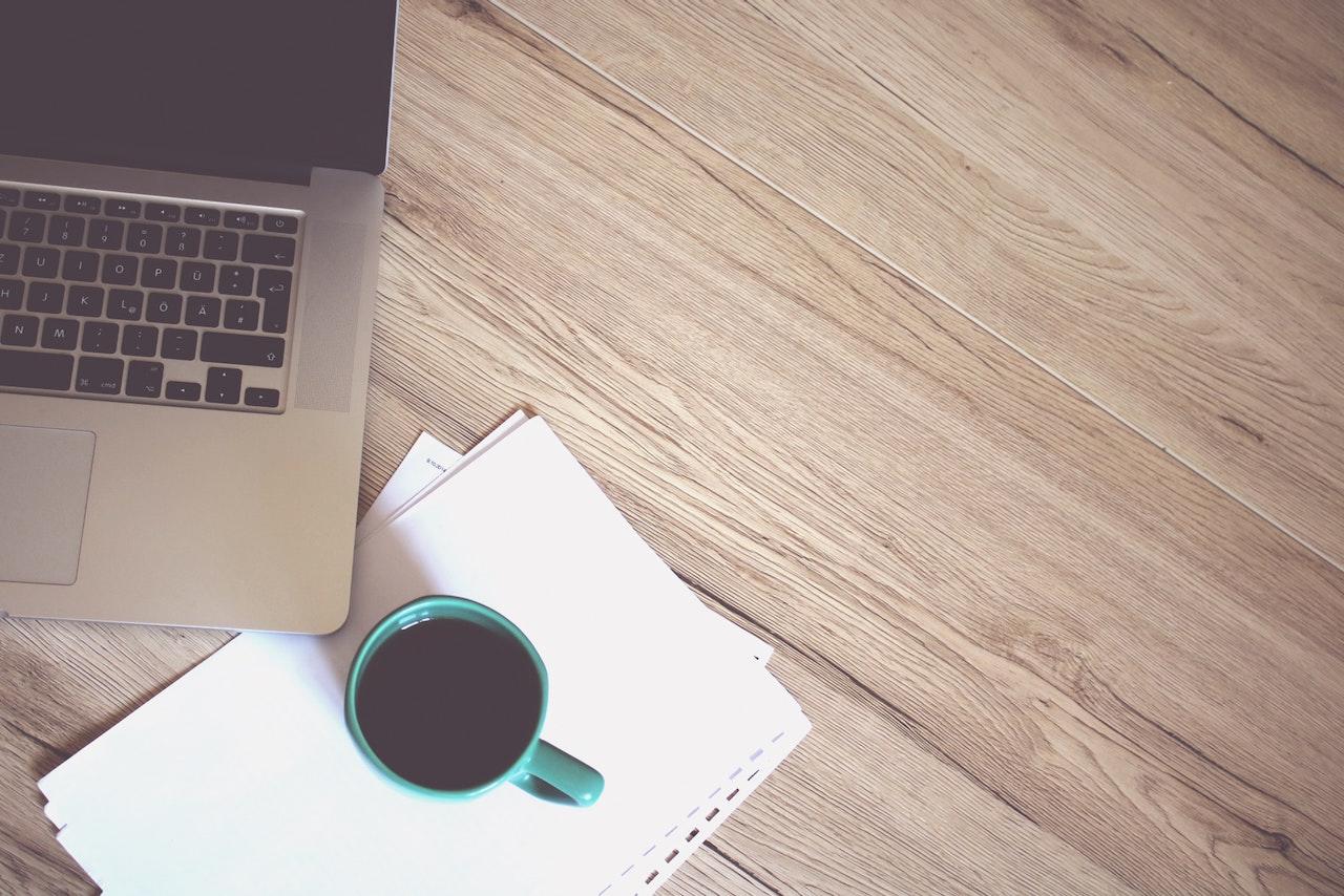 Ordinateur portable ouvert sur une table avec une tasse de café à côté posée sur des feuilles blanches.