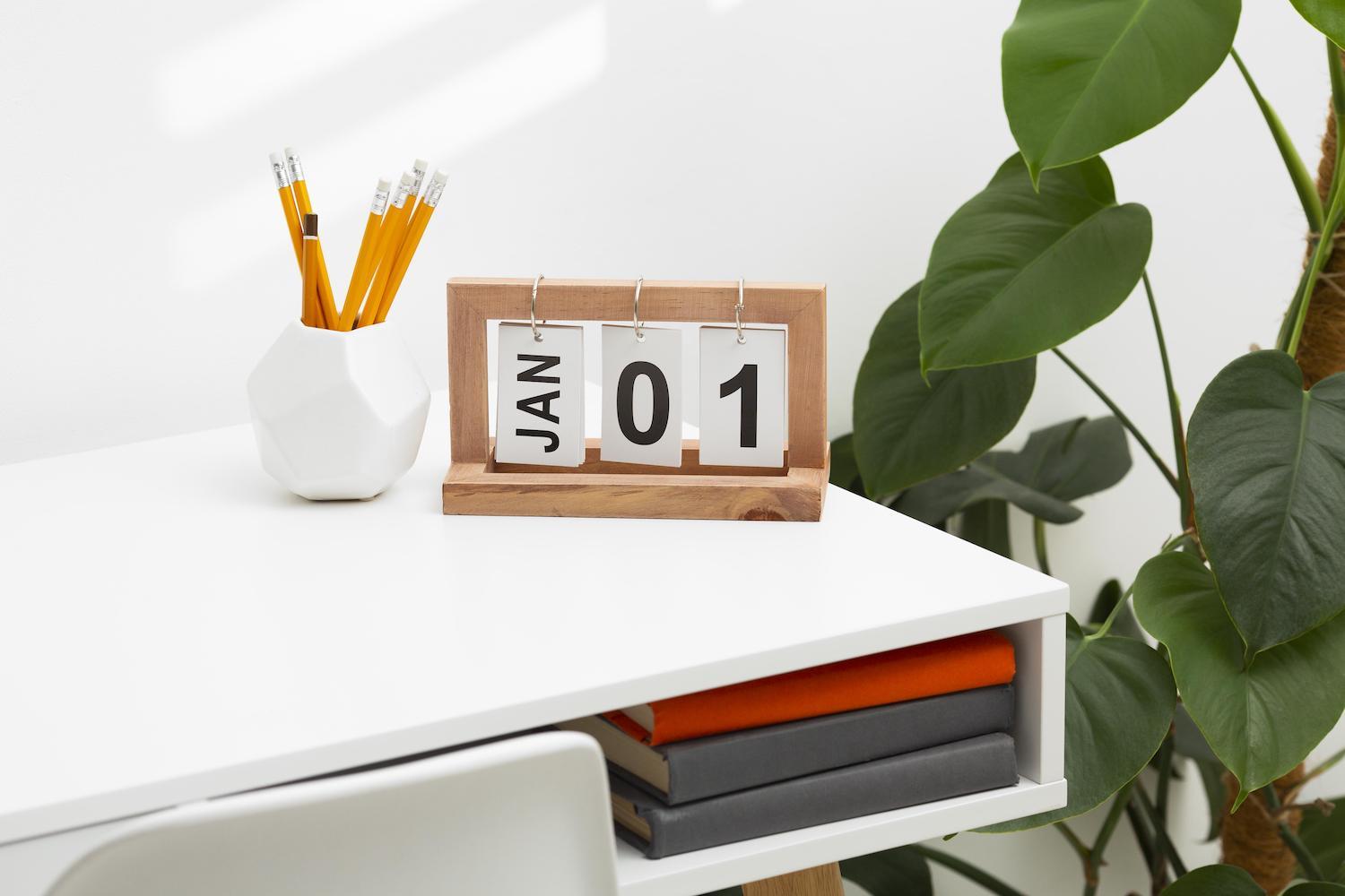 Calendrier en bois posé à côté d'un pot à crayon, plante sur la droite.