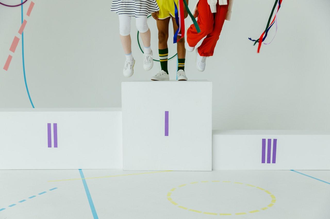 Un podium blanc avec trois enfants (on ne voit que leurs jambes) sur la première marche.