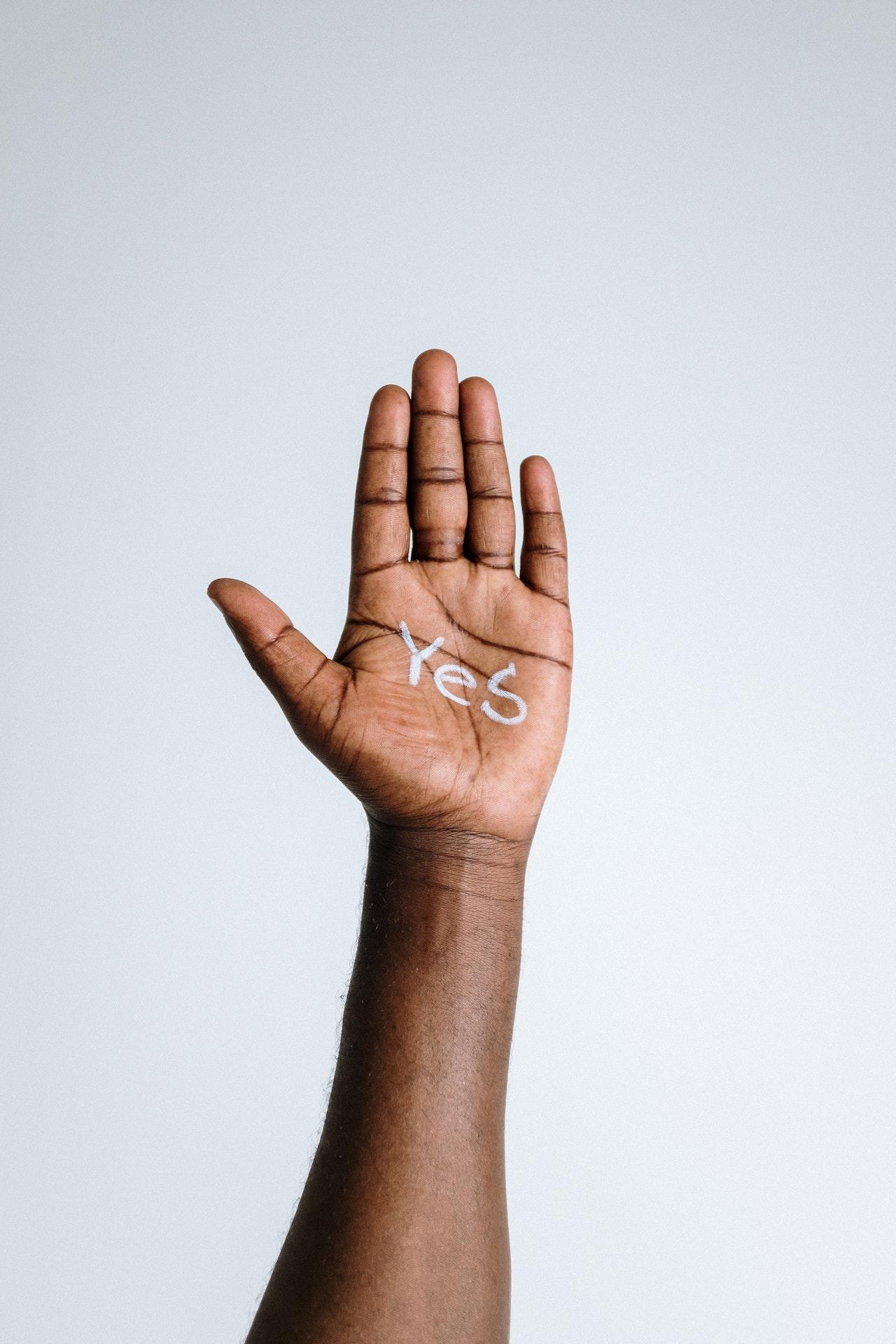 Bras noir tendu vers le haut avec la main ouverte et le mot "yes" (oui en français) écrit en blanc à l'intérieur de la paume.