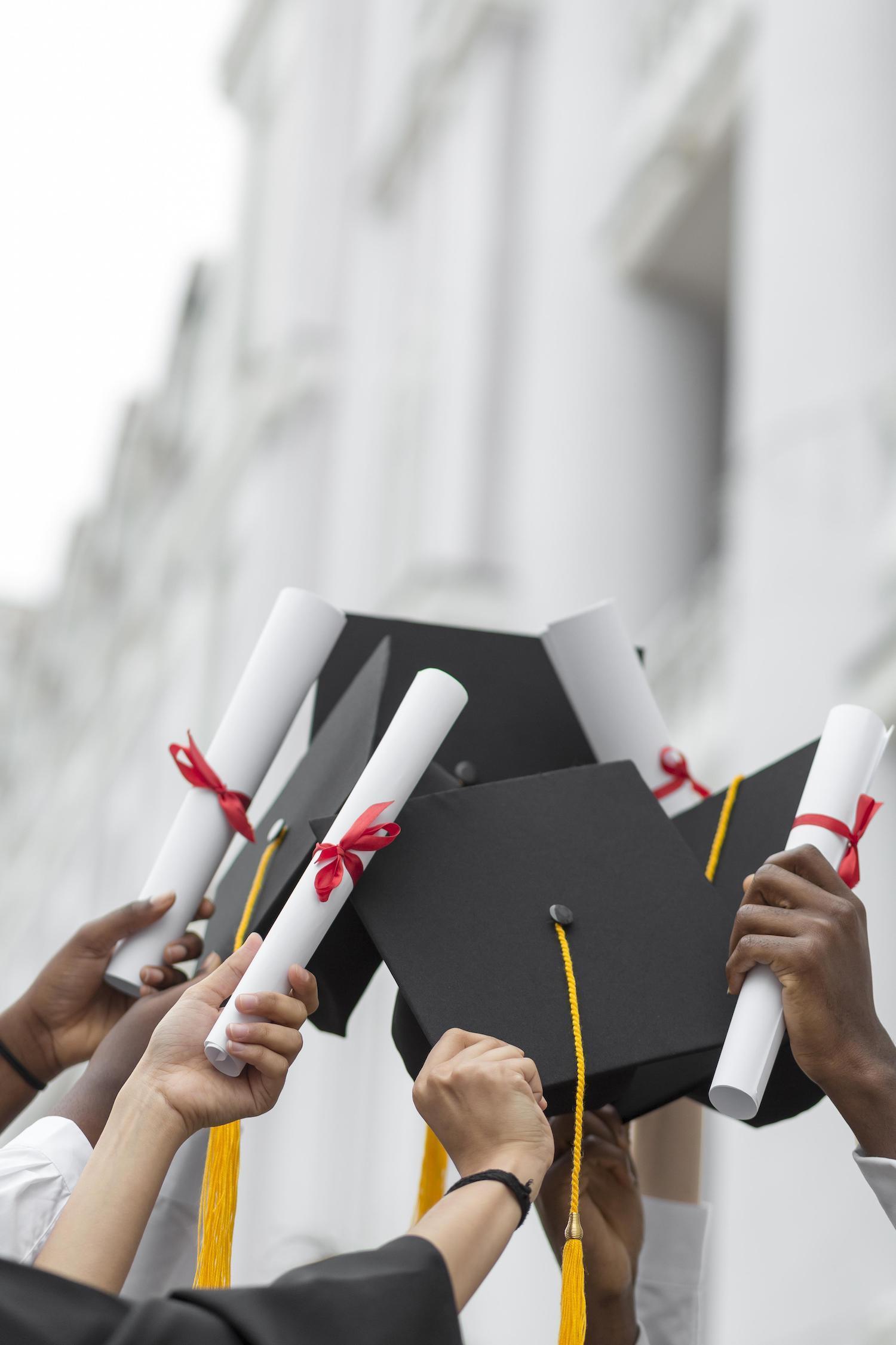 Mains de plusieurs étudiants levées tenant des diplômes et des chapeaux.