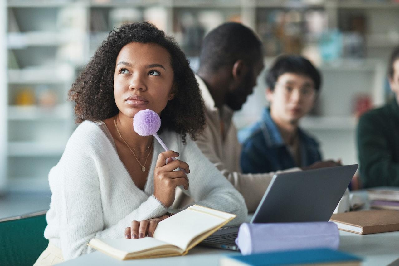 Jeune femme noire qui réfléchit un stylo à la main.