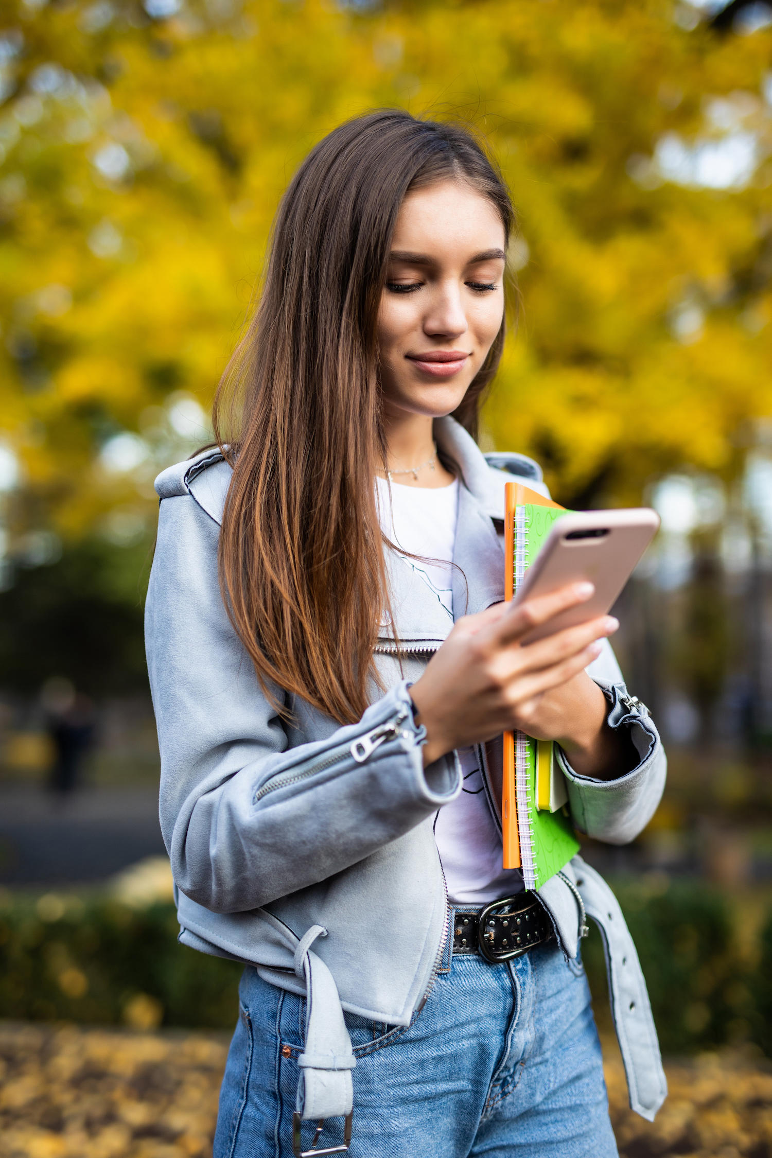 Une jeune femme porte des dossiers et regarde son smartphone à la main. 
