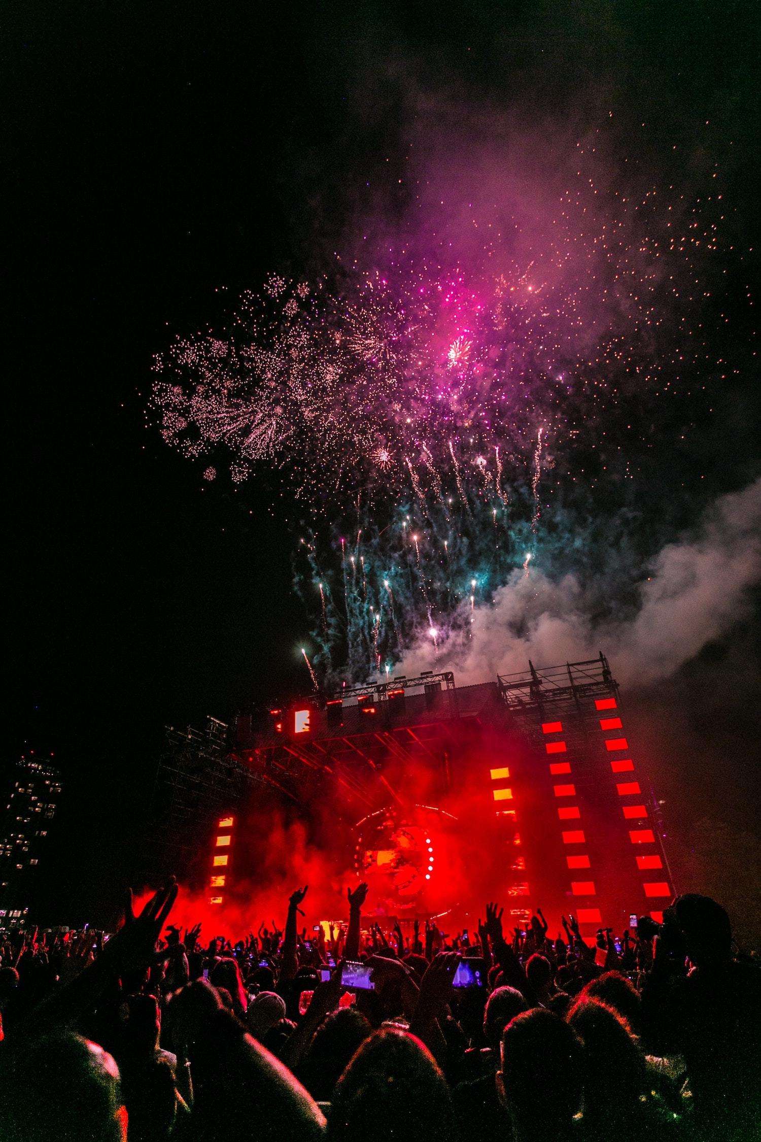 Foule devant une scène de concert avec des lumières et des feux d'artifices.