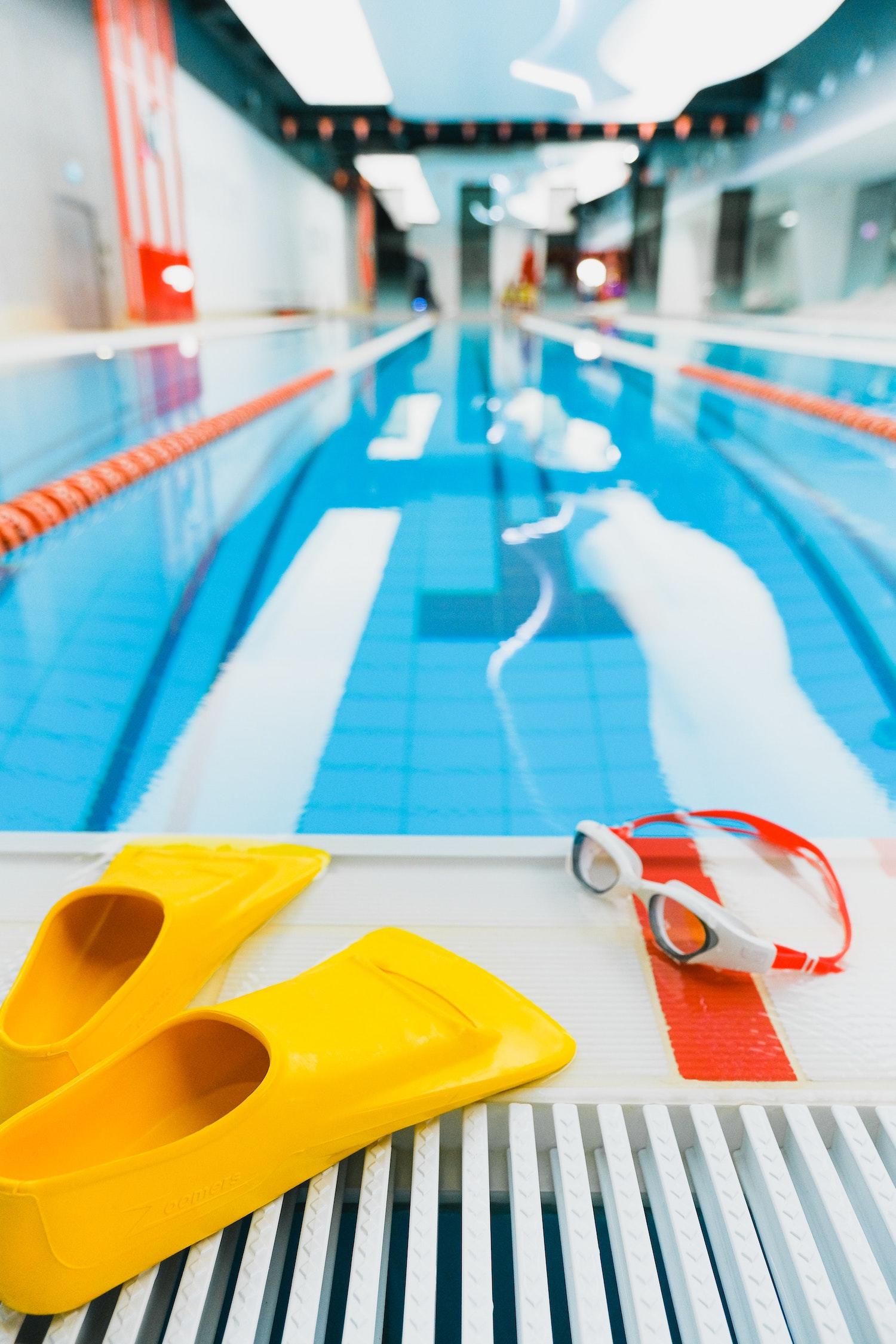 Des palmes et des lunettes sont posées sur le bord d'une piscine.
