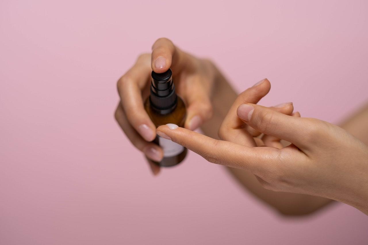 Mains de femme sur fond rose qui récupère une pression de sérum sur le doigt.