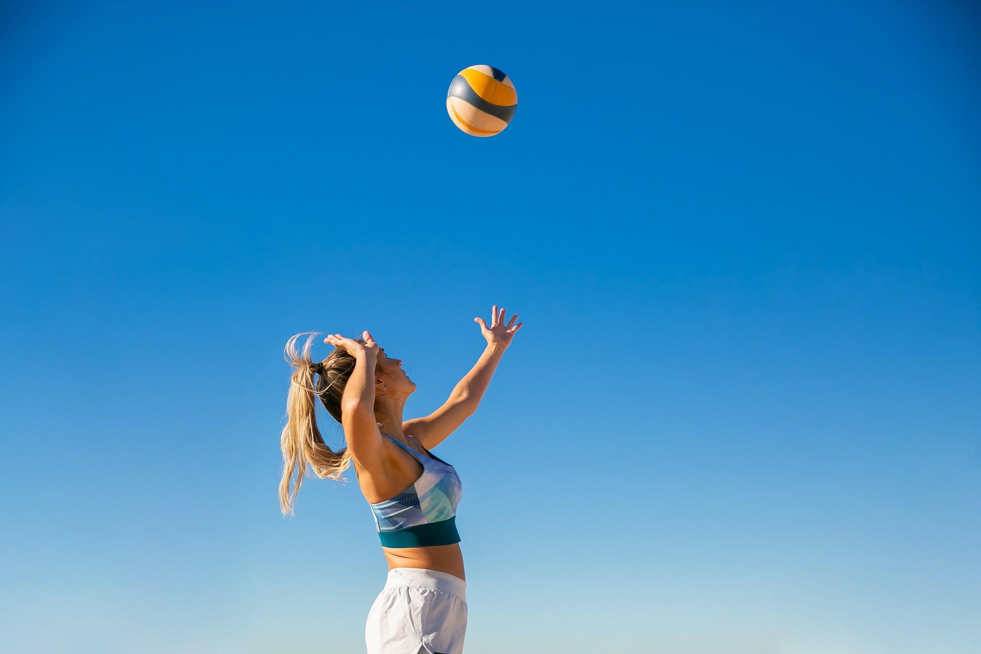 Une jeune femme exécutant un service au beach volley.