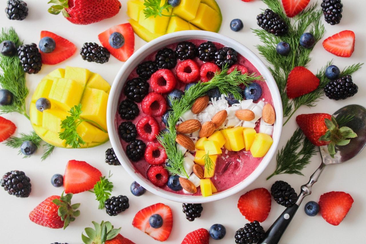 Bol rempli de fruits rouges, d'amandes, de noix de coco et de purée de fruits rouges, le tout posé sur une table avec des fruits et une cuillère
