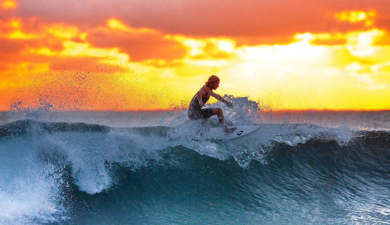 Jeune homme blond sur une planche de surf sur une vague au coucher du soleil.