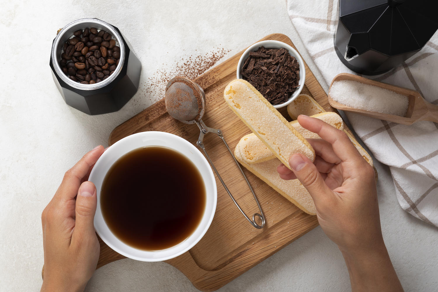 Une main tient un boudoir, à côté il y a du café et du cacao