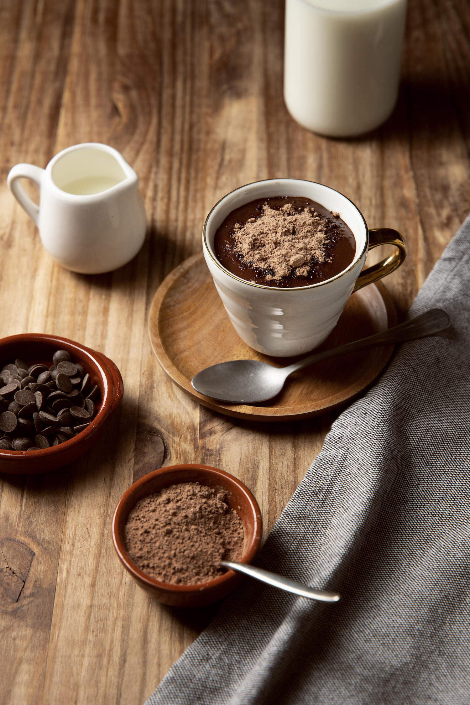 Une mousse au chocolat servie dans une petite tasse avec du chocolat en poudre et d'autres éléments autour.