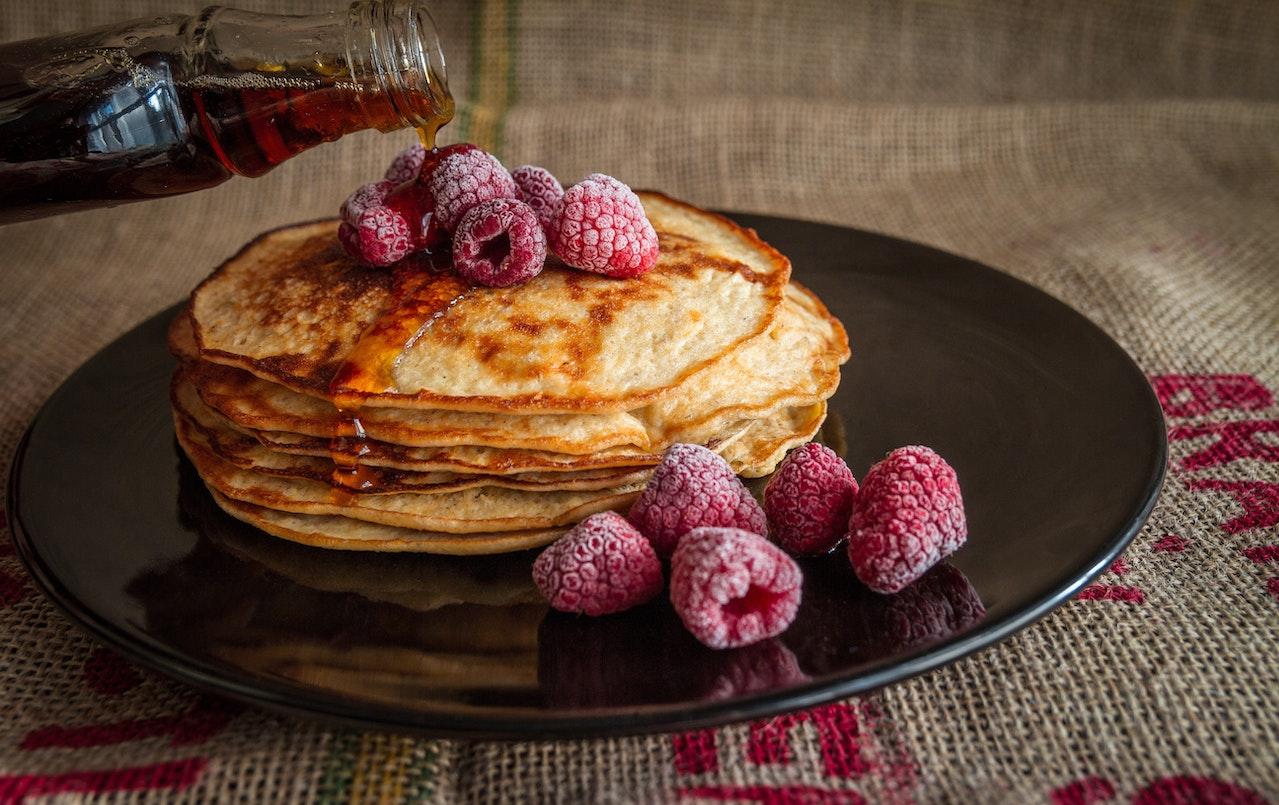 Pile de pancakes dans une assiette avec du sirop d'érable et des framboises.