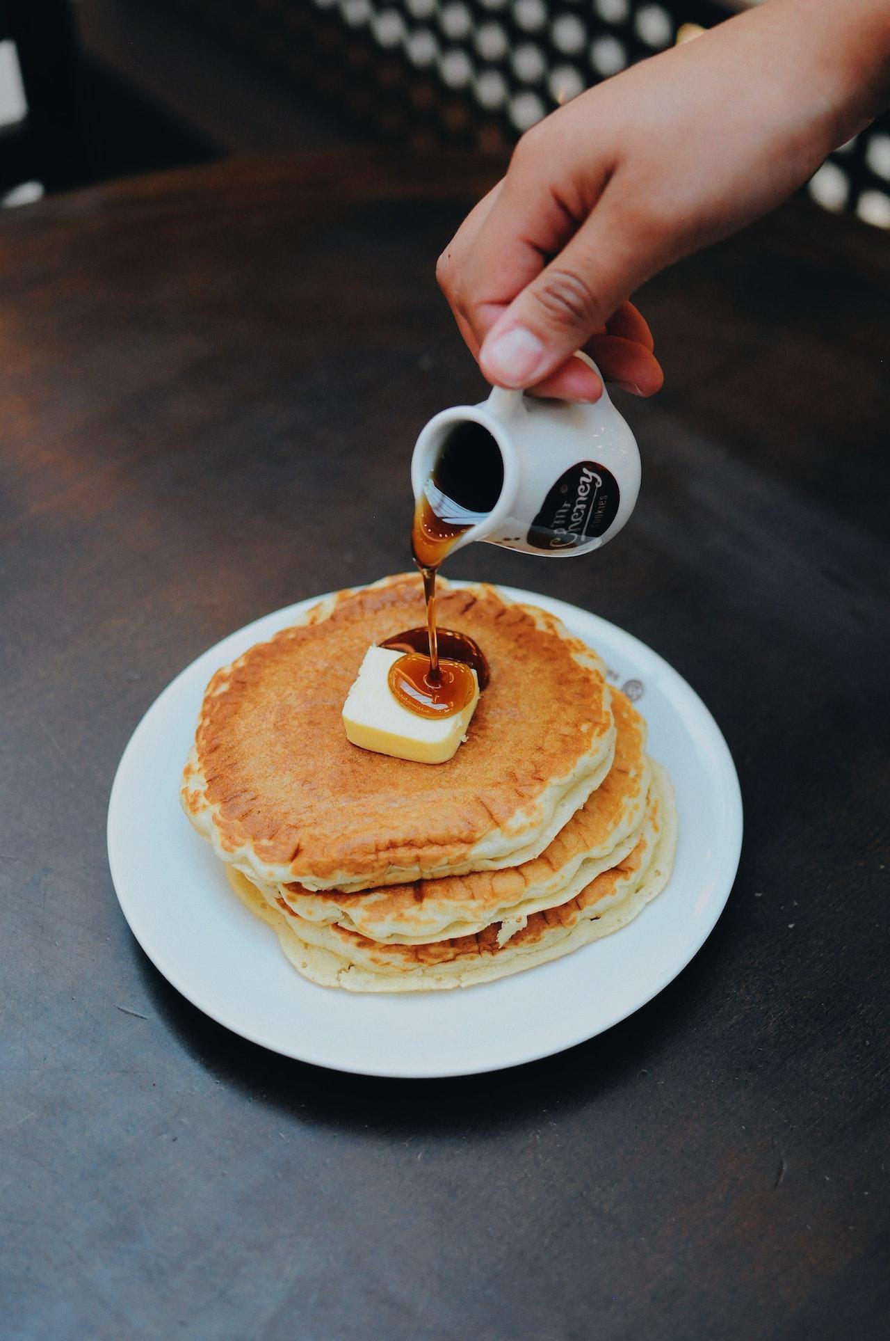 Pancakes vus d'en haut sur lesquels quelqu'un verse du sirop d'érable.