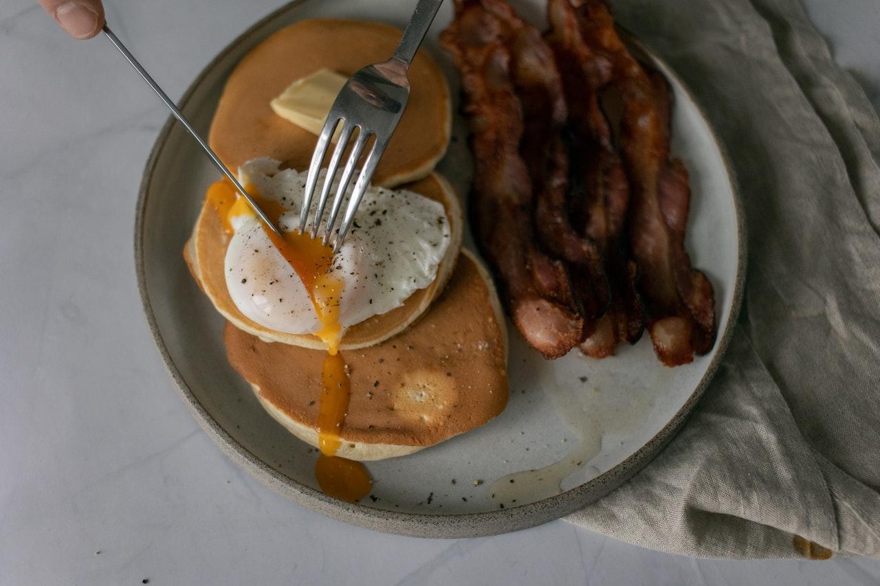 Pancakes disposés dans une assiette avec un oeuf et des tranches de bacon.