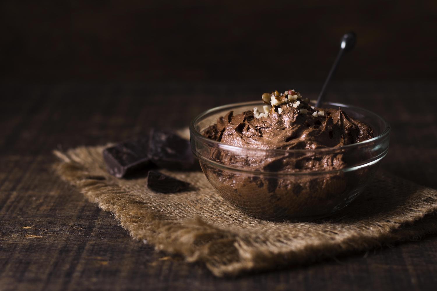 Une petite verrine de mousse au chocolat posée sur une toile de juste à côté de quelques carrés de chocolat