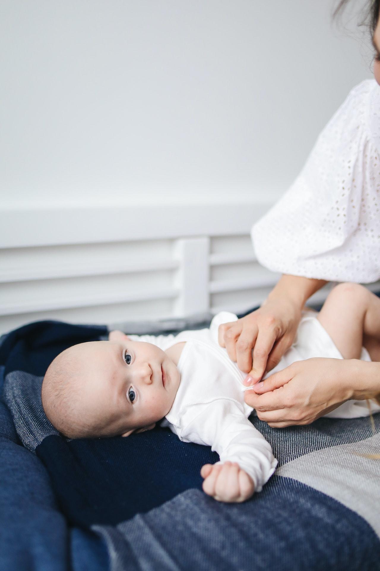Un bébé allongé sur une table à langer et une maman qui l'habille. 